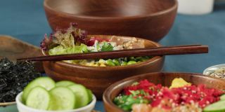 传统的夏威夷美食在餐桌上的特写。煮熟的poke碗与切片蔬菜，鱼和绿叶植物，干海藻。健康的素食。亚洲素食生食，筷子
