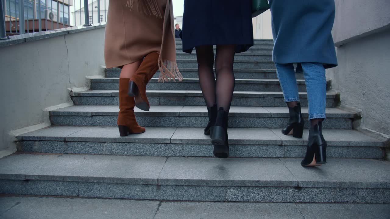 镜头跟随三个穿着秋衣的美丽快乐的女商人的双腿，在寒冷的市中心上楼梯。