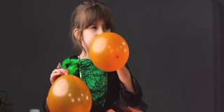 一个漂亮的小女孩穿着漂亮的裙子，嘴巴握在手里，为万圣节派对依次吹着橙色的气球。