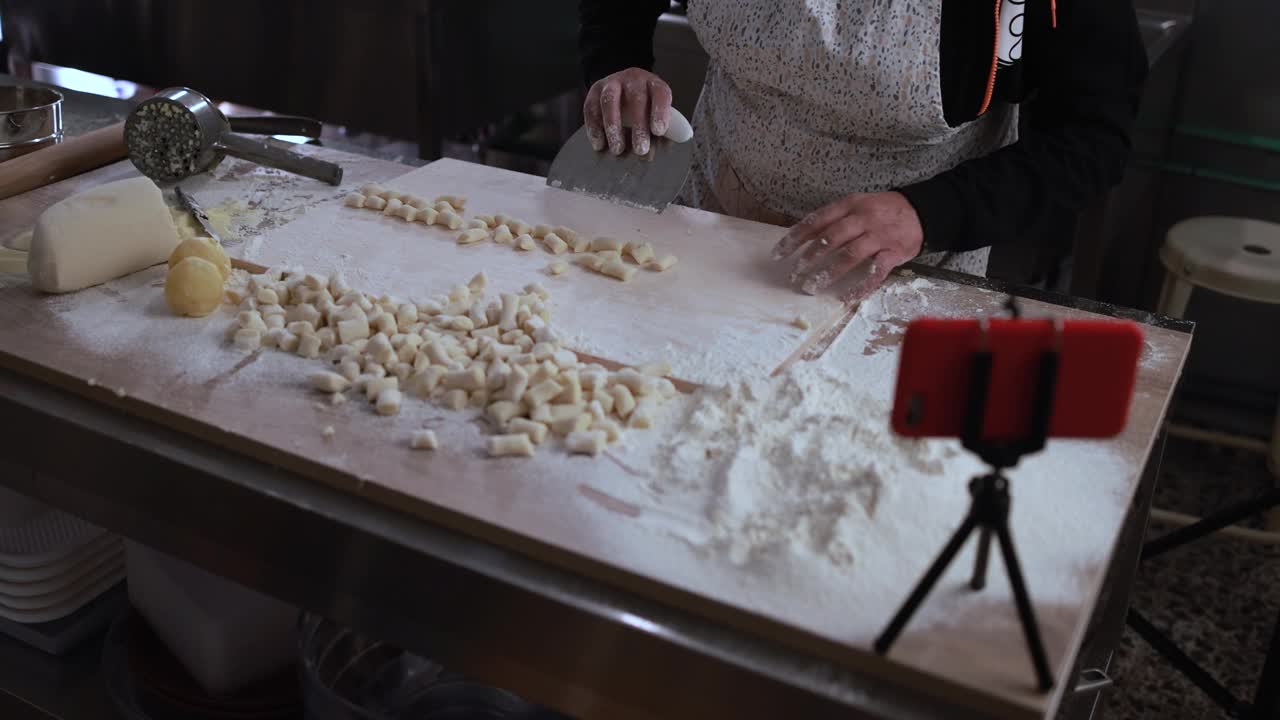 在意大利面厂内，一名妇女一边用智能手机直播视频，一边准备新鲜的意大利汤团