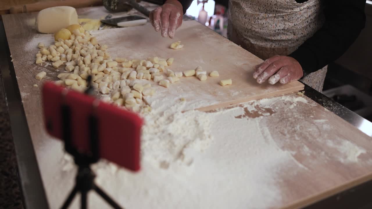 在意大利面厂内，一名妇女一边用智能手机直播视频，一边准备新鲜的意大利汤团