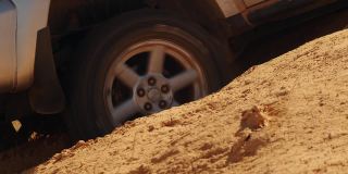特写一辆越野车车轮打滑洞在越野，侧视图。汽车被困在沙坑里，正试图离开