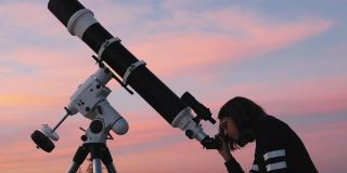 一个小女孩的剪影，望远镜在繁星点点的天空下。