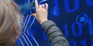 一名女子用智能手机拍摄视频蓝色背景上以二进制代码形式出现的符号，未来主义符号的灵感来自数字未来的概念