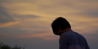 一个印度人在日落时看橙色云彩的剪影。人类仰望天空，寻找希望。孤独的概念。孤独寂寞的人仰望天空。