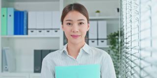 肖像的亚洲年轻聪明的女商人在公司办公室工作。美丽的女职员微笑着站在工作场所感到快乐和自信。业务概念的求职和招聘