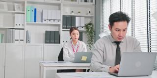 一群亚洲迷人的商业人士在办公室工作。商人和女职工坐在桌子上用笔记本电脑工作，为企业的公司项目策划。