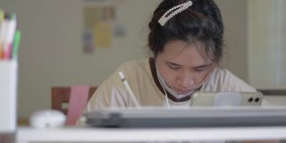 亚洲漂亮的年轻女子在休闲服装工作与数字平板电脑和笔在家里的桌子上。泰国族裔女大学生在家庭隔离的情况下在线学习有关数字设备的课程。