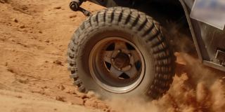 特写移动越野车行驶在沙质道路上，侧视。越野车行驶在沙漠上，尘土飞扬。在强大的越野汽车上旅行的概念