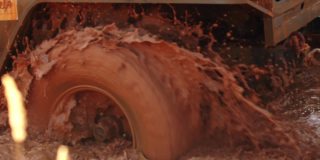 肮脏的越野车的巨大轮子卡在水坑和泥里，特写镜头。汽车在泥里打滑。越野驾驶的概念