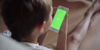 小男孩在手机上看内容。绿屏模型。带着智能手机的孩子的后视图