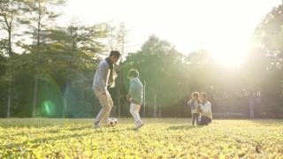 一个亚洲小男孩和爸爸在公园里踢足球视频素材模板下载