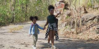非裔美国可爱的小妹妹在森林里徒步旅行。两个黑人女孩在野外旅行。一群小学生背着书包，手牵着手在公园里散步。