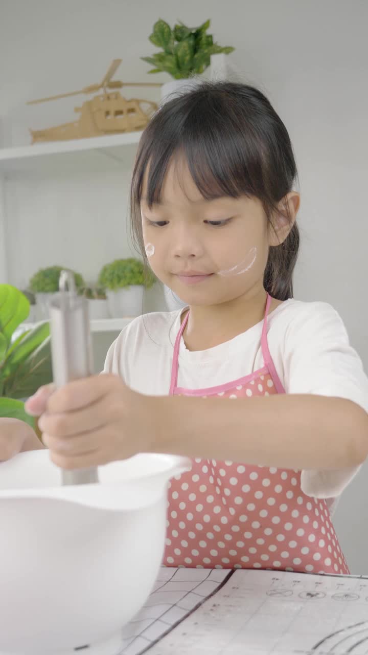 快乐的亚洲孩子在家里学习做饼干，女孩在搅拌碗里搅拌面粉。