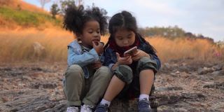 不同的孩子朋友非洲裔美国人和亚洲女孩一起使用智能手机在自然的山上与阳光。一群孩子在花园公园用手机玩互联网。