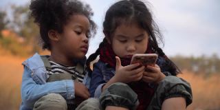 不同的孩子朋友非洲裔美国人和亚洲女孩一起使用智能手机在自然的山上与阳光。一群孩子在花园公园用手机玩互联网。