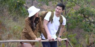 快乐的亚洲年轻夫妇与背包游客走在山路上的小径。相爱的两个人在大自然中徒步旅行。
