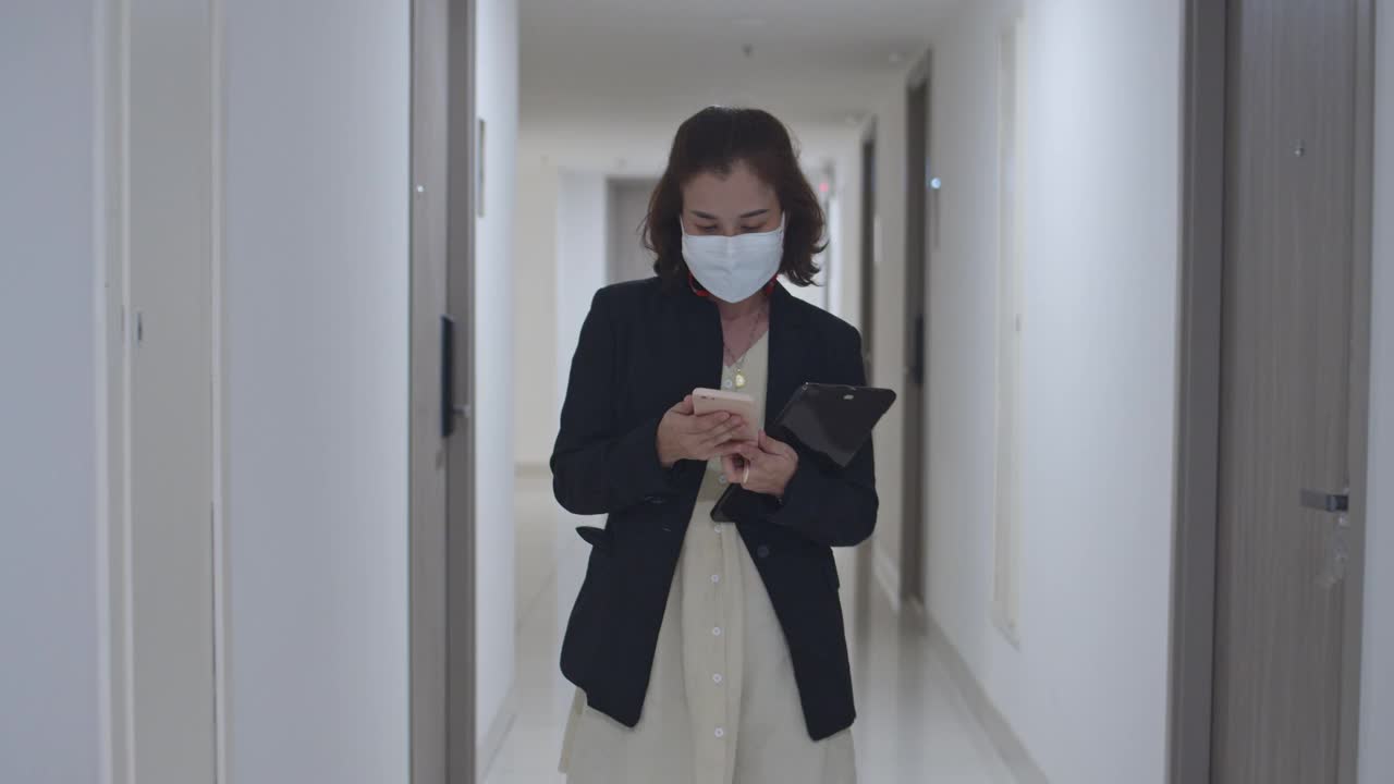 女商人戴着医用口罩走路，用智能手机，慢动作