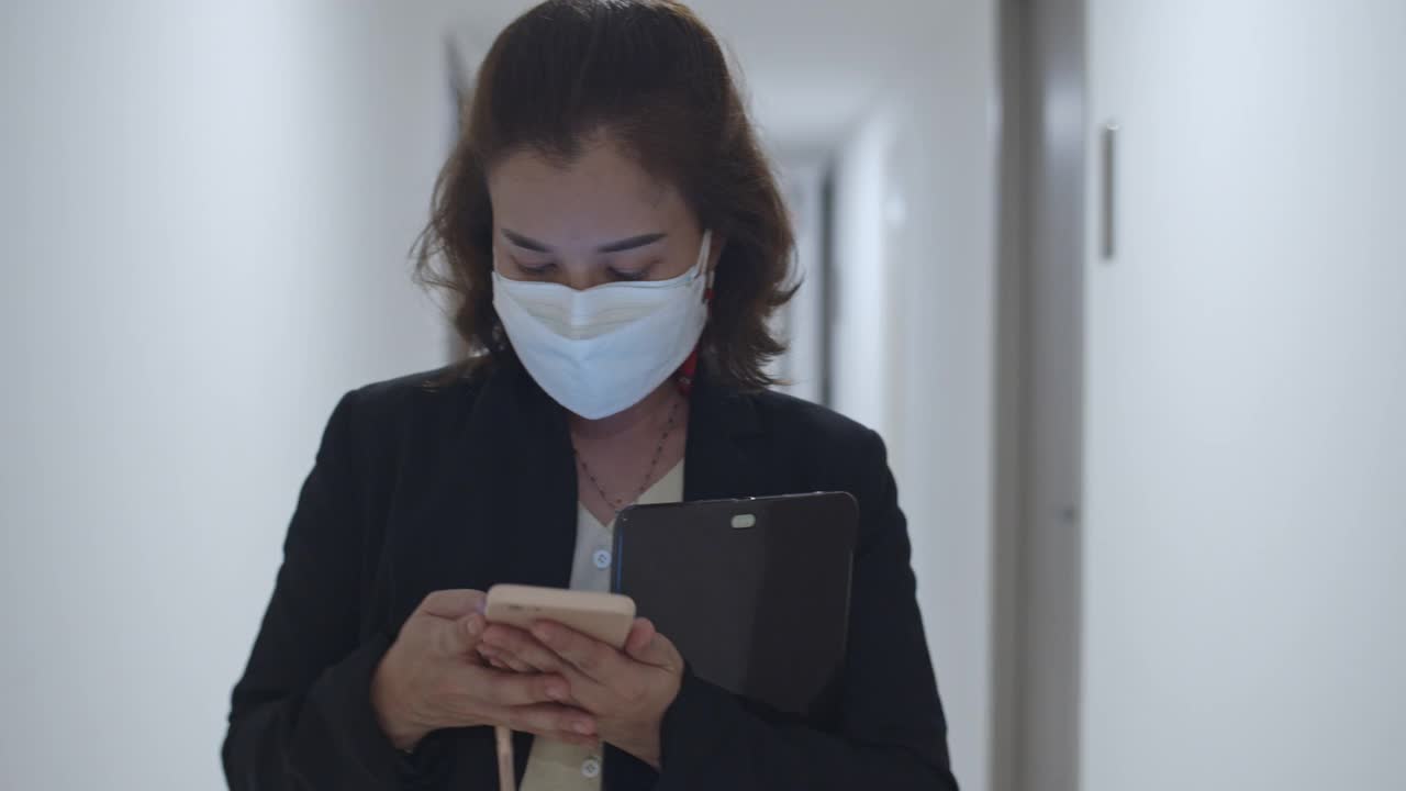 SLO MO女商人戴着外科口罩走路，使用智能手机，关闭
