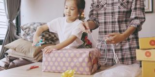5岁的亚洲女孩和她的妈妈正在用漂亮的纸盒包装礼物，庆祝节日(圣诞节、新年和生日)，显示出家人在一起的快乐和对他人的问候。