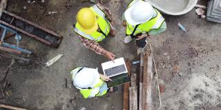 一群工程师穿着反光背心，戴着安全安全帽在建筑工地工作。建筑工程师作为一个工作团队一起工作的鸟瞰图