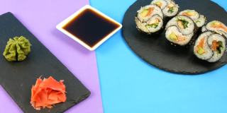 黑色的棒子带阴阳寿司卷，有鳗鱼和红色的鱼鲑鱼，时髦的紫色背景板黑色的板，绿色的山葵和粉红色的姜。极简主义风格的日本料理