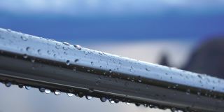 不锈钢扶手上的雨滴映衬着模糊的大海背景。特写镜头。雨露的水滴聚集在闪闪发光的铬钢杆扶手上
