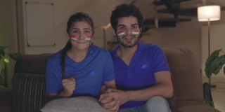 一对年轻的印度夫妇在电视机前观看、欢呼和享受板球比赛。