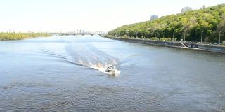 汽船沿着宽阔的城市河流疾驶。一艘白色的摩托艇漂浮在蓝色的河面上，浪花飞溅。