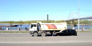 乌克兰基辅——2021年4月24日:汽车沿着路堤高速公路行驶。背景中，一艘货轮顺流而下。城市繁忙道路上的交通。
