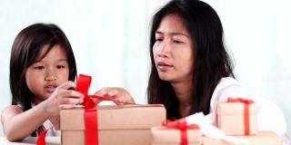年轻的亚洲母亲和女儿帮助包装乡村礼品盒礼物领带红色丝带蝴蝶结。赠送的季节，圣诞节，新年快乐，生日，情人节，周年纪念日，母亲节。