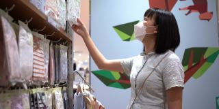 亚洲妇女带着防护口罩在婴儿用品店购买婴儿服装