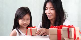 小亚洲可爱的小女孩与妈妈激动地打开礼品盒礼物领带与红色丝带蝴蝶结在家里。圣诞节，新年快乐，生日，情人节，母亲节。