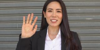 POV:微笑的亚洲女商人挥手欢迎顾客或同事。视频电话会议。远程工作的概念