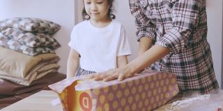 5岁的亚洲女孩和她的妈妈正在用漂亮的纸盒包装礼物，庆祝节日(圣诞节、新年和生日)，显示出家人在一起的快乐和对他人的问候。