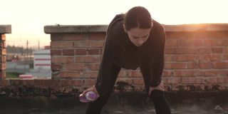 女运动员运动后，拿着一瓶水疲惫地站在屋顶上
