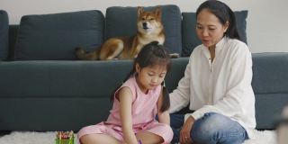 亚洲母亲和女儿和他们的狗一起画画。家庭室内休息。