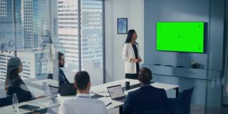 多元化办公室会议室会议:亚洲成功女企业家演讲，用绿屏彩色键墙电视向投资者展示产品。电子商务战略。广角镜头
