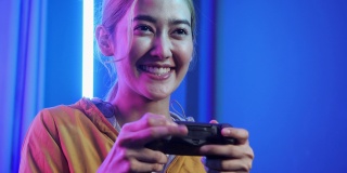 亚洲年轻女性在家玩网络游戏。玩游戏的女孩在控制电子游戏的操纵杆。十几岁的女孩在家里的霓虹灯房间里休闲游戏。