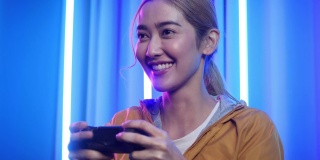 亚洲年轻女性在家玩网络游戏。玩游戏的女孩在控制电子游戏的操纵杆。十几岁的女孩在家里的霓虹灯房间里休闲游戏。