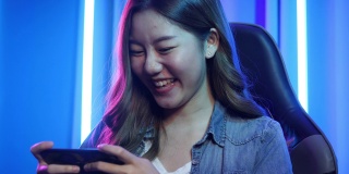 亚洲年轻女子在智能手机上玩在线游戏。游戏玩家女孩控制智能手机视频游戏。十几岁的女孩在家里的霓虹灯房间里休闲游戏。