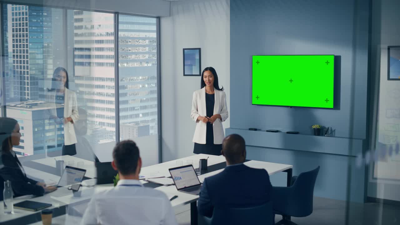 办公室会议室会议介绍:亚洲女商人谈话，使用绿屏彩色键墙电视。成功地向众多投资者展示产品。商人们鼓掌