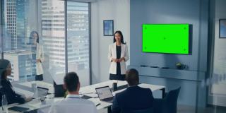 办公室会议室会议介绍:亚洲女商人谈话，使用绿屏彩色键墙电视。成功地向众多投资者展示产品。商人们鼓掌