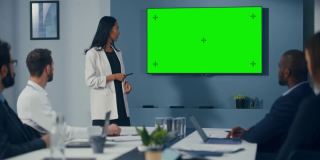 办公室会议室会议介绍:积极的商人谈话，使用绿色屏幕彩色键墙电视。成功向多民族投资者群体展示电子商务产品