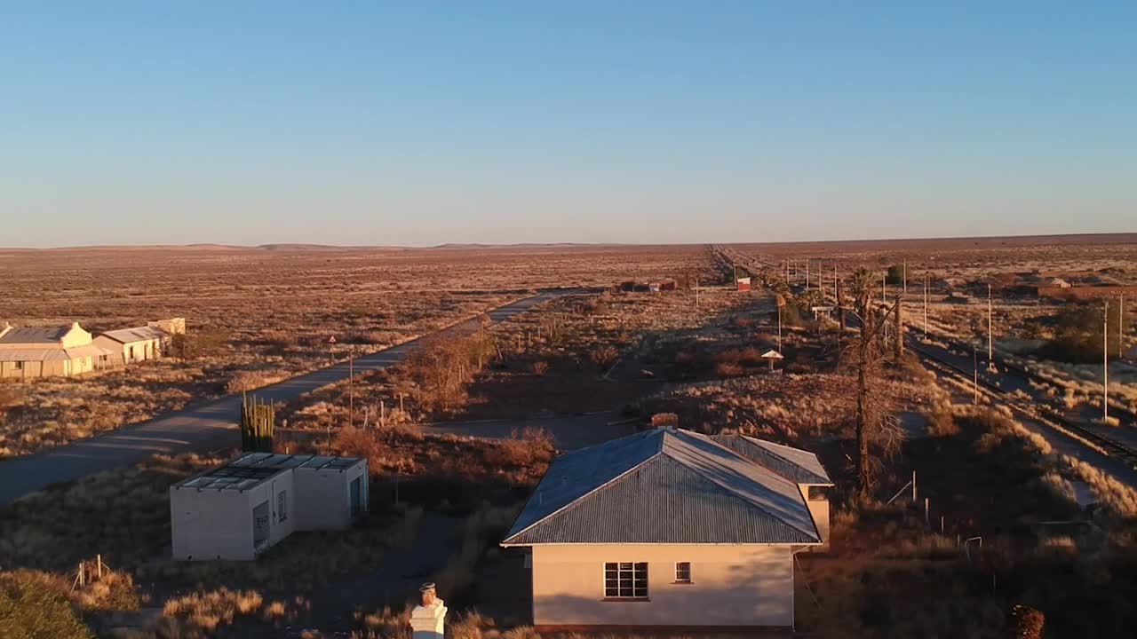 石子路与铁轨平行，长长的阴影笼罩着建筑物和黄色的草地