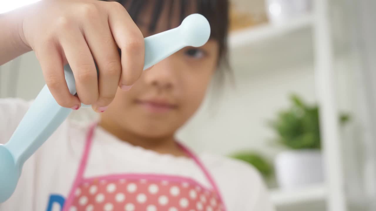 亚洲女孩在家里烘烤前用量匙准备盐。