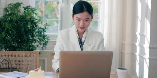 年轻的商业女性一边用笔记本电脑工作一边喝咖啡