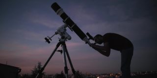 一个人的剪影，望远镜和星空下的乡村。