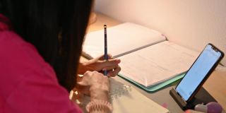 亚洲女性通过智能手机在线学习，并在家里的桌子上记笔记