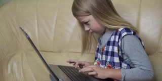 一个金发的学龄女孩正在她的笔记本电脑上打字。使用文字聊天通信。